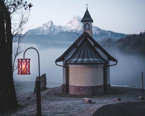 Kapelle mit Kuppeldach, umgeben von Nebel und schneebedeckten Bergen im Hintergrund.