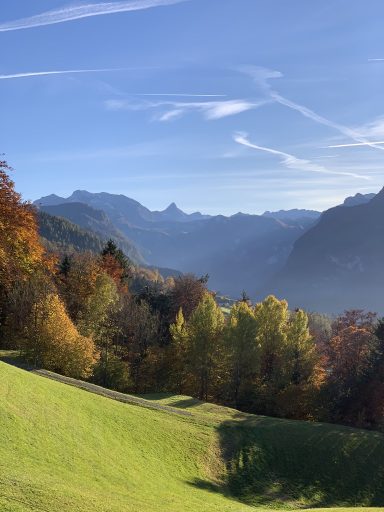 Herbstliche Landschaft mit bunten Bäumen und Bergpanorama im Hintergrund.