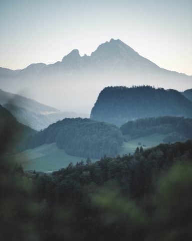 Berglandschaft mit sanften Hügeln und Nebel über den Gipfeln im Hintergrund.