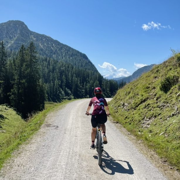 E-Bike Tour auf die Kallbrunnalm nahe Ramsau bei Berchtesgaden Fahrradfahrerin auf einem Schotterweg auf dem Weg zur Kallbrunnalm, umgeben von Bergen und Bäumen.